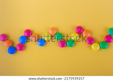 Top view on pattern made of different color round chocolate buttons lay in zigzag shape on yellow background