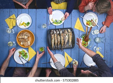 Top View On People Eating Grilled Fish With Vegetable Salad And Drinking Vine.