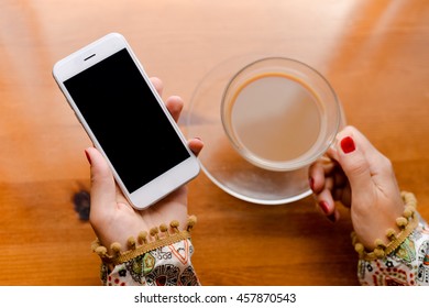 Top view on person working on mobile phone, hands and coffee cup on wooden desk background.
