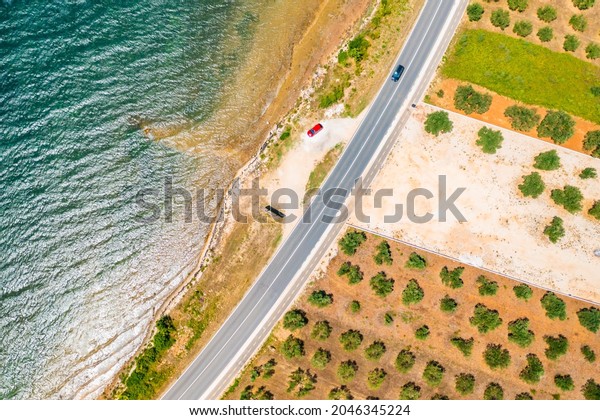 Top view on the red car parking\
near the beach of Adriatic sea and field with fruit trees.\
