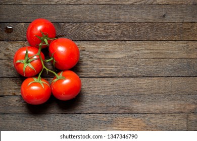 Top view on red washed tomatoes on wooden background with copy space. Left position. Group of five fresh vegetables on green branch with water droplets on it. Burnt oak wooden texture. Raw foods.