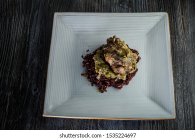 Top View On Restaurant Dish Of Whole Grilled Quail With Green Onion Dressing Served On Wild Rice On Modern Plate On Dark Wooden Table