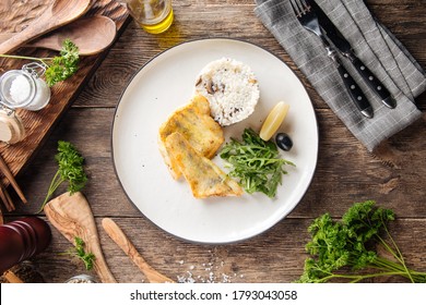 Top View On Roasted White Fish Fillet With Rice And Arugula On A White Plate