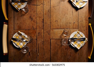 Top View On Rustic Wooden Table With Distressed Surface, Served For Simple Holiday Dinner, With Empty Plates And Wine Glasses Ans Napkins. Different Fancy Vintage Chairs On Sides.