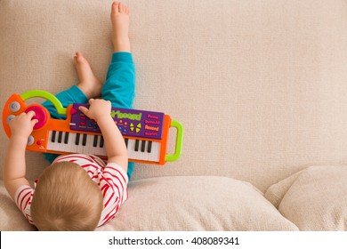 Top view on small cute toddler boy sitting on the sofa and playing on the toy piano. A little boy learning to play piano listening to music. Early development for toddler. Musical education for kids