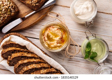 Top view on three different spreading sauces in glass jars with cut whole wheat bread on wooden boards