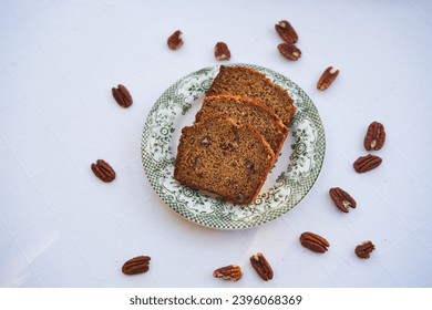 Top view on three slices of homemade banana bread with pecan nuts on the small porcelain plate isolated on the table with white table colth. Healthy, lowcarb and balanced dish ideal for breakfast. 