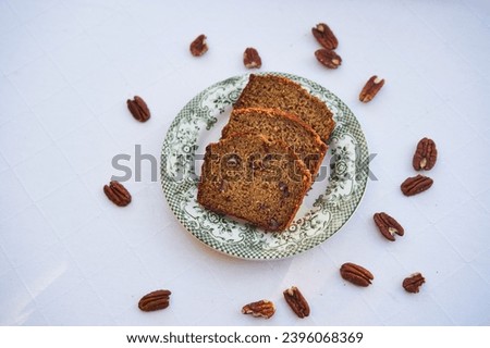 Top view on three slices of homemade banana bread with pecan nuts on the small porcelain plate isolated on the table with white table colth. Healthy, lowcarb and balanced dish ideal for breakfast. 