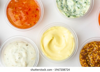 Top view on various sauces in small cups on white background. Mayonnaise, sweet and sour, cheese, tartar sauces and mustard.