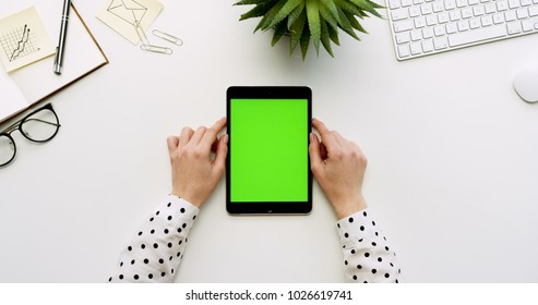 Top view on the white office desk and black tablet computer with green screen and female hands taping on it. Vertical. Office stuff beside. Chroma key. - Powered by Shutterstock