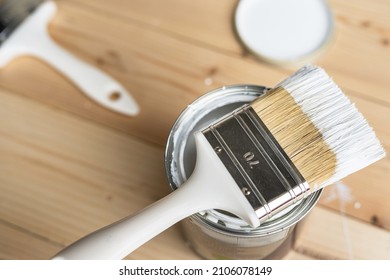 Top view on white paint brush on the opened can on the wooden table or floor painting and renovation repairing concept - Shutterstock ID 2106078149