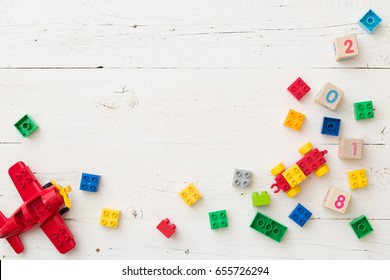 Top view on wooden cubes with numbers and colorful toy bricks and  plane on white wooden background. Toys in the table