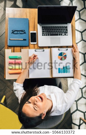 Top view on young female sitting for office desk with laptop and documents. Happy Woman smiling at her workplace.