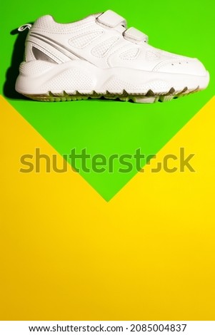 top view one white running shoes on top on a geometric paper green and yellow background with copy space, a spring and summer concept.