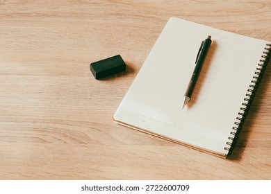 Top view of an open blank notebook with a mechanical pencil and black eraser on a wooden desk, featuring large copy space for design.