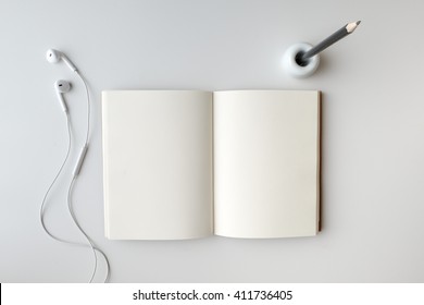 Top View Open Blank Notebook, Earphone, And Pencil In Holder On White Desk Background