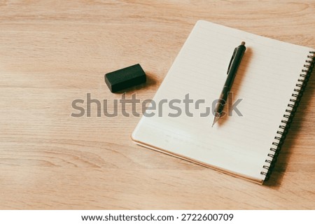 Top view of an open blank notebook with a mechanical pencil and black eraser on a wooden desk, featuring large copy space for design.