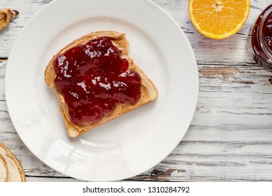 Top view of open face homemade peanut butter and strawberry Jelly sandwich on oat bread, over a white rustic wooden table / background. Served with fresh oranges / fruit.
