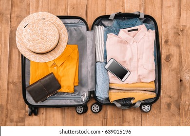 Top View Of Open Luggage Full Of Clothes, Document And Smartphone On Wooden Floor, Summer Travel Concept