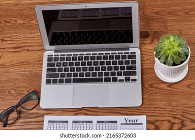Top view open macbook air laptop pc with glasses and plant. Brown wooden desk background.