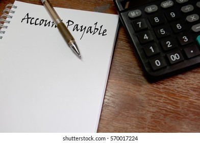 Top view of open notebook written with ACCOUNT PAYABLE inscription. Calculator, pen and notebook on wooden background. Business & Accountancy Concept.  