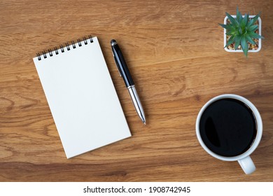 Top view of open school notebook with blank pages, coffee cup and pen for taking write notes on wood table background. Flat lay, creative workspace office. Business-education concept with copy space.