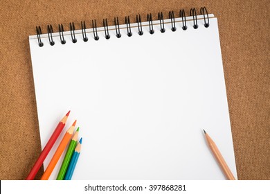 Top View Of Open Spiral Sketchbook With Colored Pencils On Brown Background