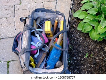 Top View Of Open Tool Bag On Stone Walkway Beside Garden Bed. Home Repairs