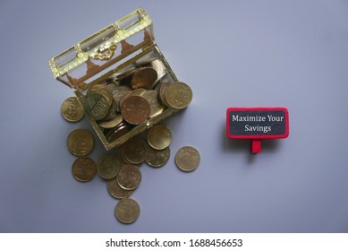 Top View Of Open Treasury Box Full With Gold Coins And Wooden Notice Board Written With Maximize Your Savings On A Gray Background.