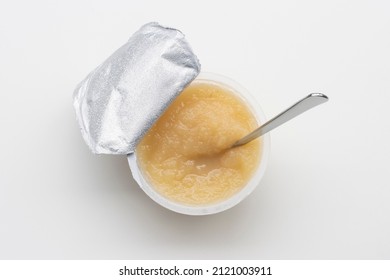 Top View Of An Opened Cup Of Unsweetened Applesauce With A Spoon In It, Isolated On A White Background. Gluten-free Vegan Kids Snack.