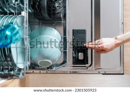 Top view of opened dishwasher machine with plastic detergent compartment and chemical tablet. Washing tableware. Full loaded rack. Modern appliance in kitchen