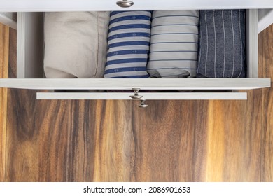 Top View Of Opened Drawers Of White Dresser And Rolled Shirts In It.Empty Wooden Floor Indoors