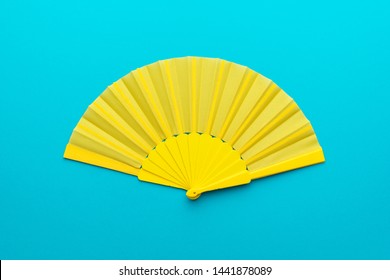 Vista superior de la maqueta abierta del ventilador amarillo sobre fondo azul turquesa. Fotografía plana minimalista del ventilador plegable con composición central.