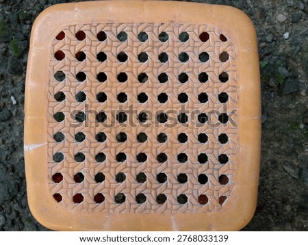 Top view of an orange plastic stool with a perforated geometric pattern on a rocky ground background.