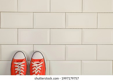 Top View Of Orange Tennis Shoes On White Tile Wall.