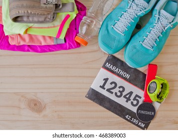 Top view of outfit for runner on wooden background: bib number, finisher medal, bottle of water, gps watch, running shoes, running waist bag, shorts, shirt, and sport bra. Horizontal orientation. - Powered by Shutterstock