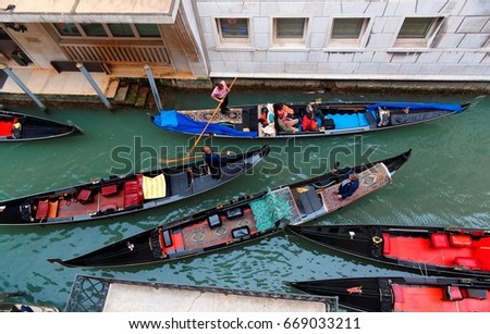 Top view over a narrow alley in Venice, a romantic city in Italy, with gondoliers steering beautiful gondolas with single oars and making their way thru the busy canal flanked by old historical houses