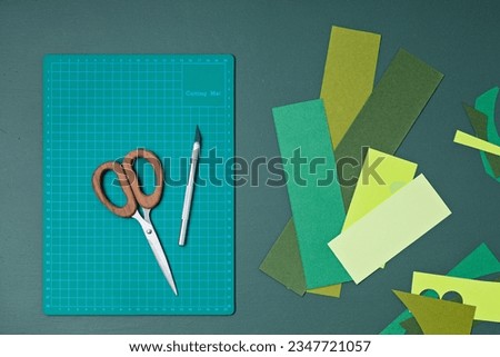 Top view over paper cut tools, scissors, cutter, cutting mat, and crafted paper objects. DIY trendy project concept. Flat lay
