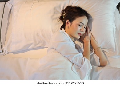 Top View Oversleeping Asian Woman Wearing White Sleepwear Lying Or Sleeping In Bed In Bedroom With Happiness And Smile Face While Having Good Dream. Lifestyle Concept