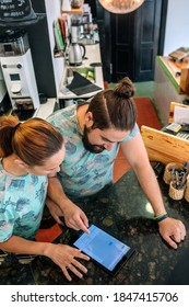 Top View Of Owners Of A Coffee Shop Working Looking At The Tablet Leaning On The Counter