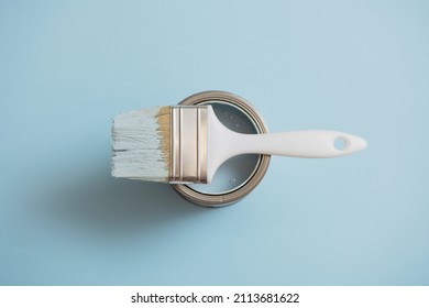 Top view of paint brush lying on open can of blue paint on blue background.