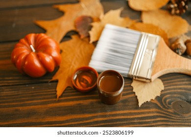 Top view of a paintbrush placed on dried autumn leaves with acorns, pine cones, and a pumpkin on a rustic wooden background. - Powered by Shutterstock