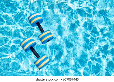 Top view - pair of dumbbells for aqua aerobics float on the surface of water in swimming pool on a warm summer day