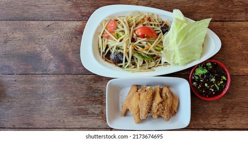 Top view of papaya salad, pickled crab, spicy Thai food, papaya salad seasoned with lime juice, tomato, pepper, fish sauce and sugar, served on a white plate with fried chicken and sweet dipping sauce