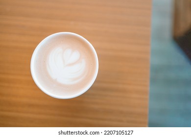 Top View Of Paper Cup Of Cappuccino Coffee With Latte Art On Wooden Table In Cafe. 