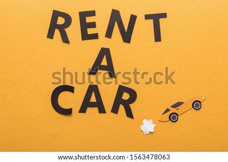 top view of paper cut sports car with exhaust gas and black rent a car lettering on orange background