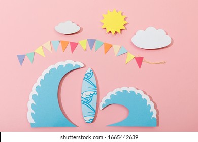 Top View Of Paper Cut Sun, Clouds, Flags, Surfboard And Sea Waves On Pink Background