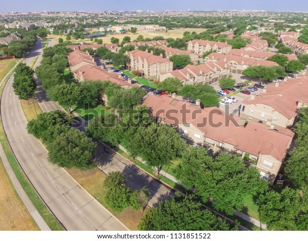 Top view park side\
apartment and residential house near local street in Irving, Texas,\
USA. Aerial view covered parking lots, cars and trees at\
multi-floor buildings\
complex