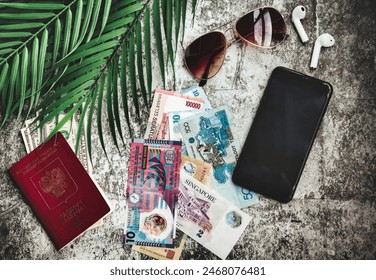 Top view of passport, currency, sunglasses, smartphone, and palm leaf on desk, suggesting preparation for journey. Travel essentials on textured surface. Travel vacation concept. Copy ad text space - Powered by Shutterstock