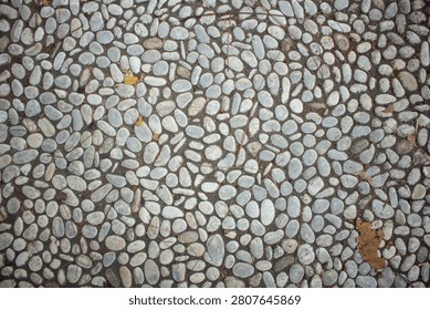 Top view of a path made of natural white oval pebbles and round river stones arranged neatly in a concrete garden walkway texture.